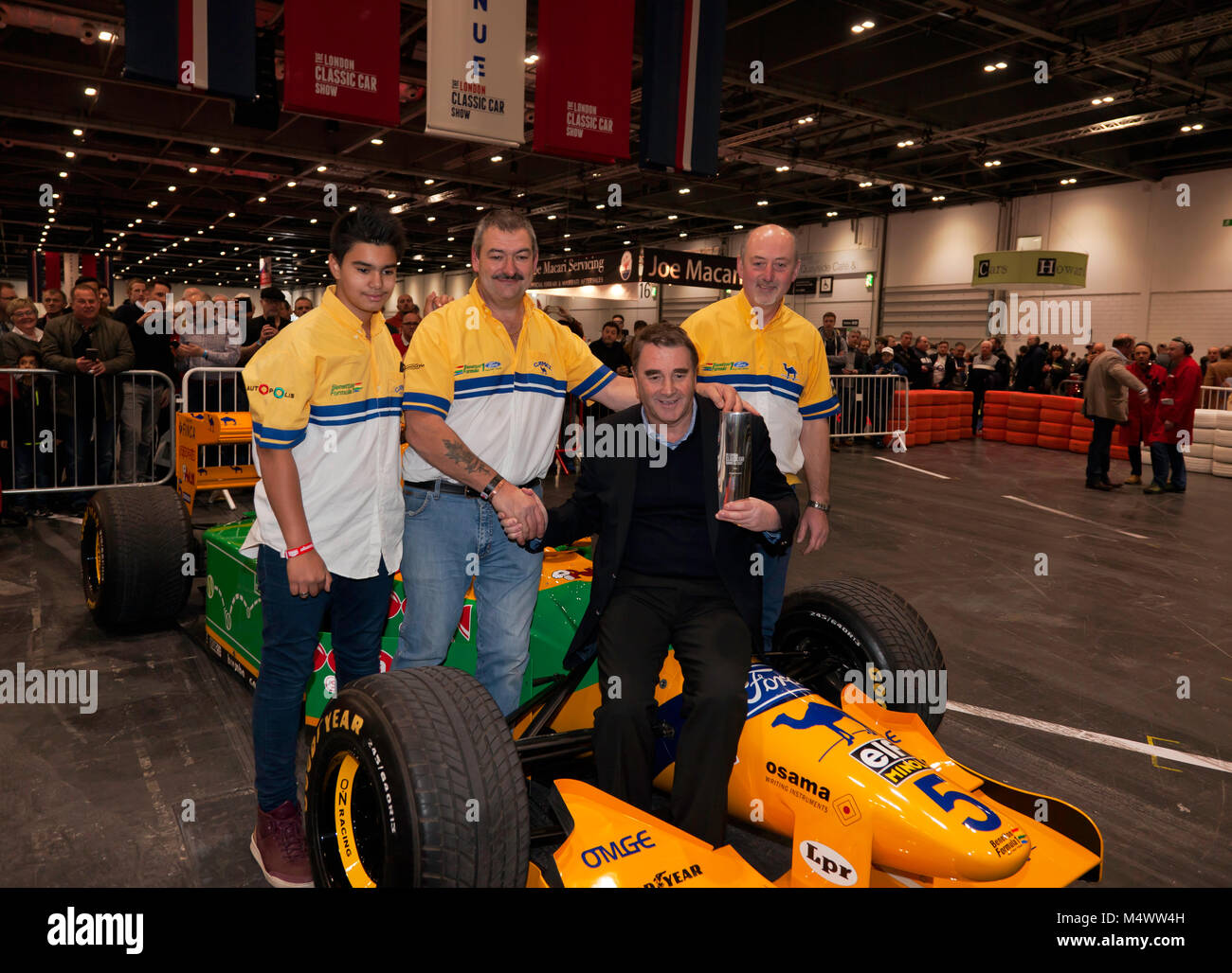 Nigel Mansell CBE, surrounded by the Benetton F1 Team Mechanics,  posing with the London Classic Car Show 'Icon' award in the Grand Avenue, after his drive in the Benetton 193B F1 car Stock Photo