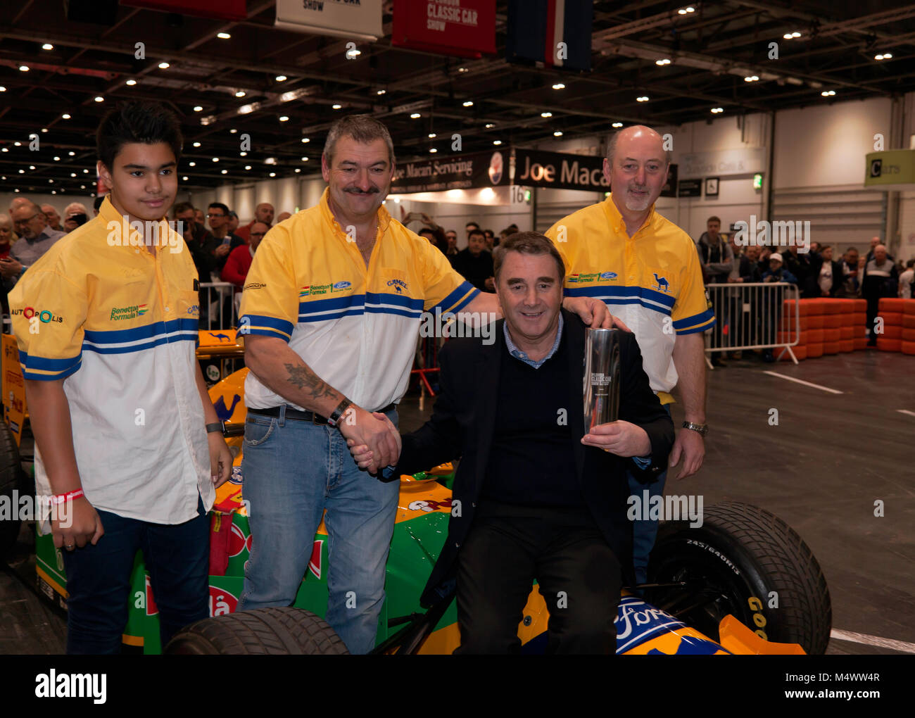 Nigel Mansell CBE, surrounded by the Benetton F1 Team Mechanics,  posing with the London Classic Car Show 'Icon' award in the Grand Avenue, after his drive in the Benetton 193B F1 car Stock Photo