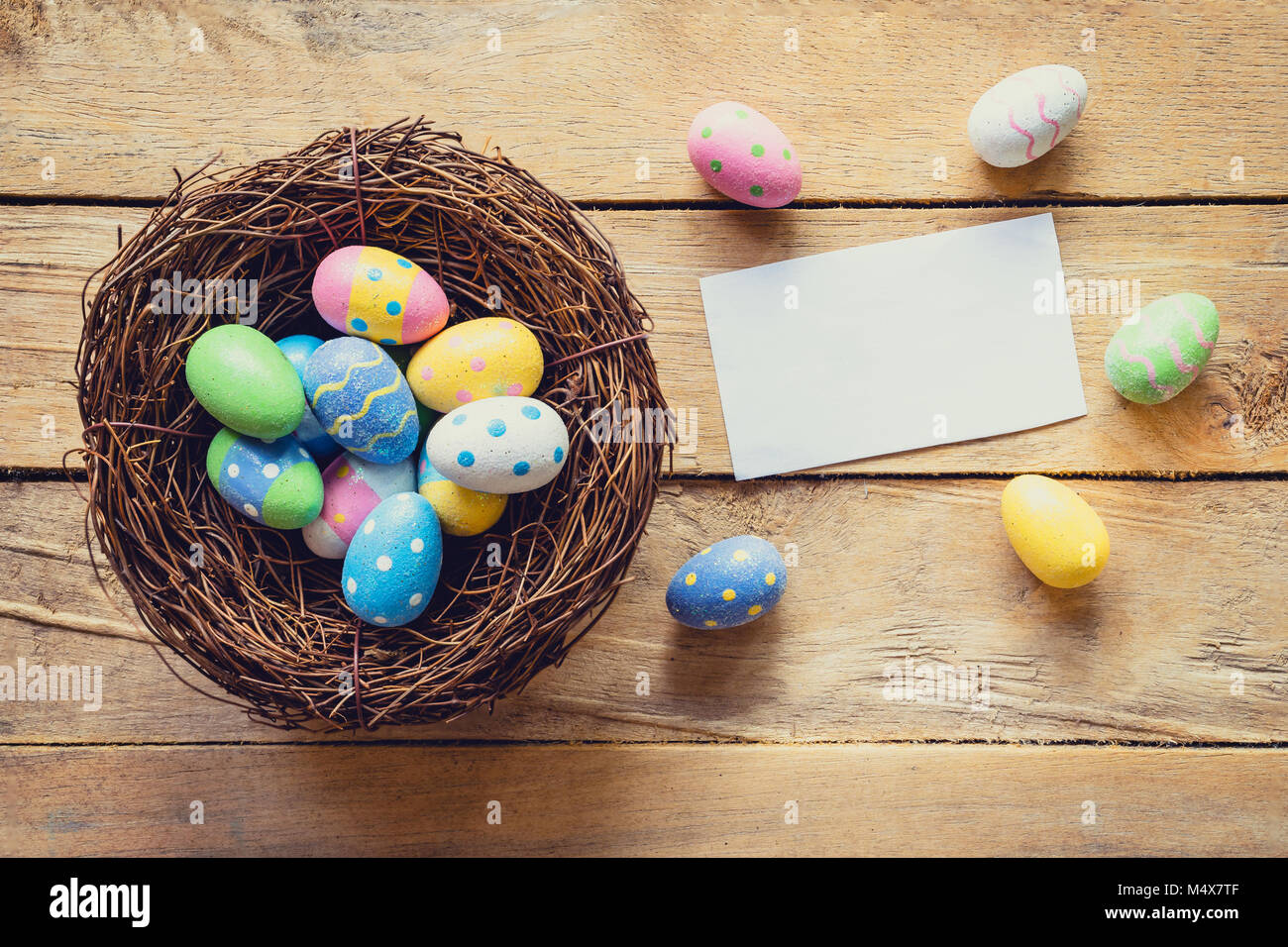 Colorful easter egg in nest and paper card on wood background with ...