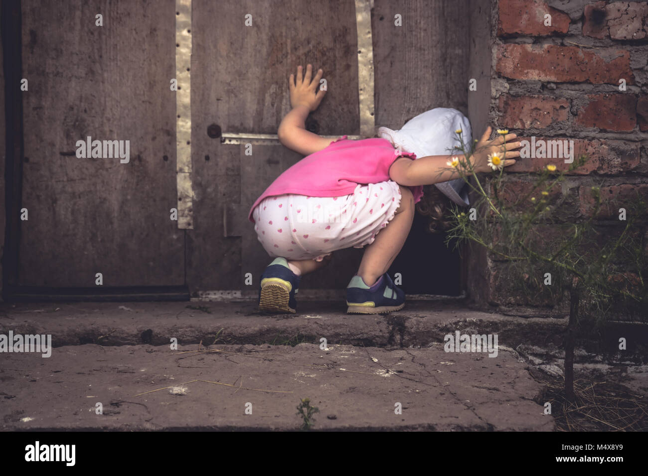 Curious child looking into dark hole in barn door in countryside shed concept curiosity Stock Photo