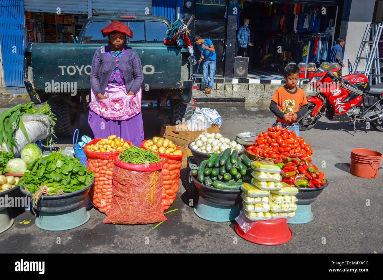 A Guatemalan woman wearing traditional dress and a young boy sell vegetables on a street market. Stock Photo