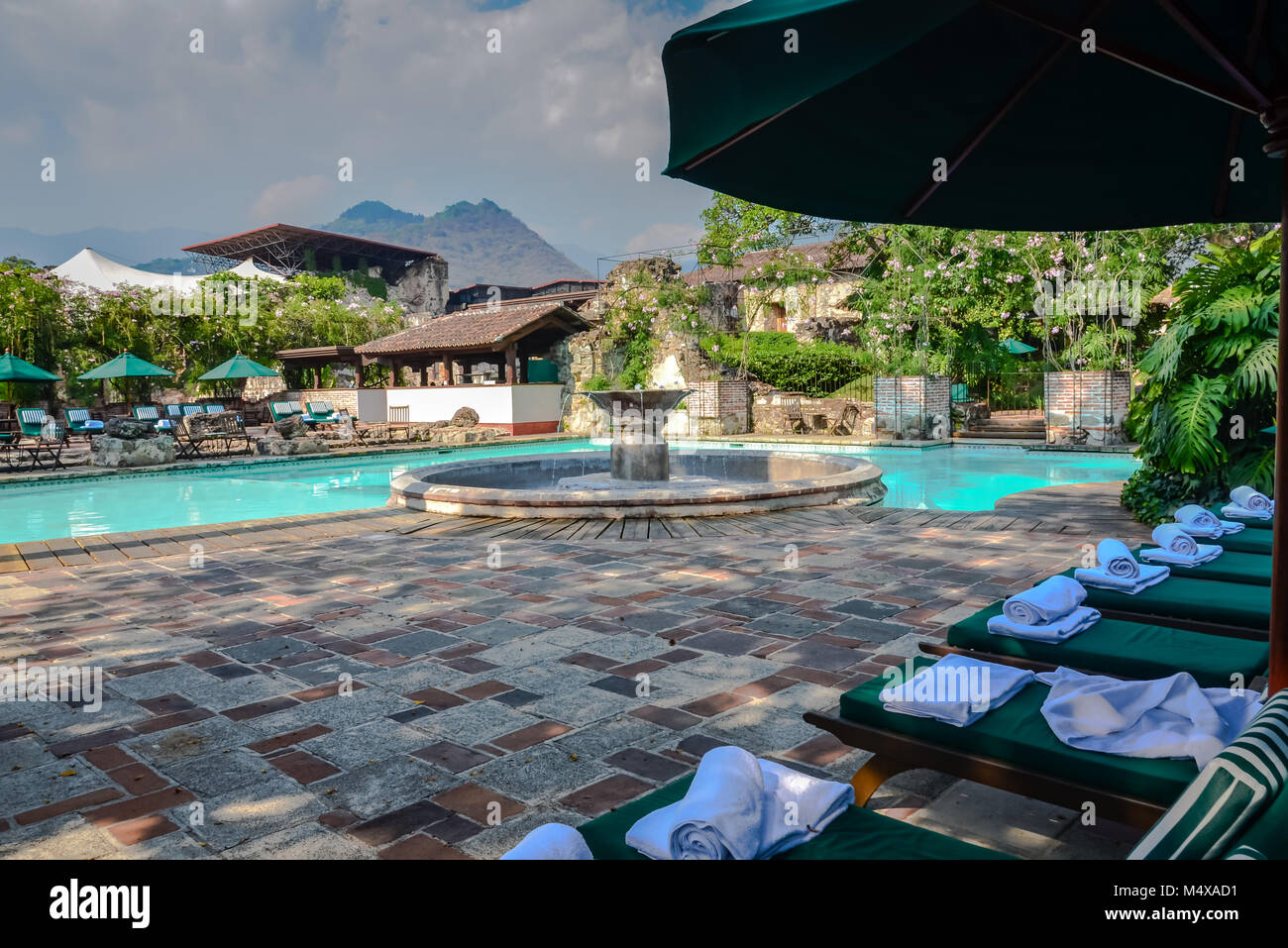 Antigua, Guatemala. Old world elegance at a resort pool with a central fountain and a row of green lounge chairs. Stock Photo