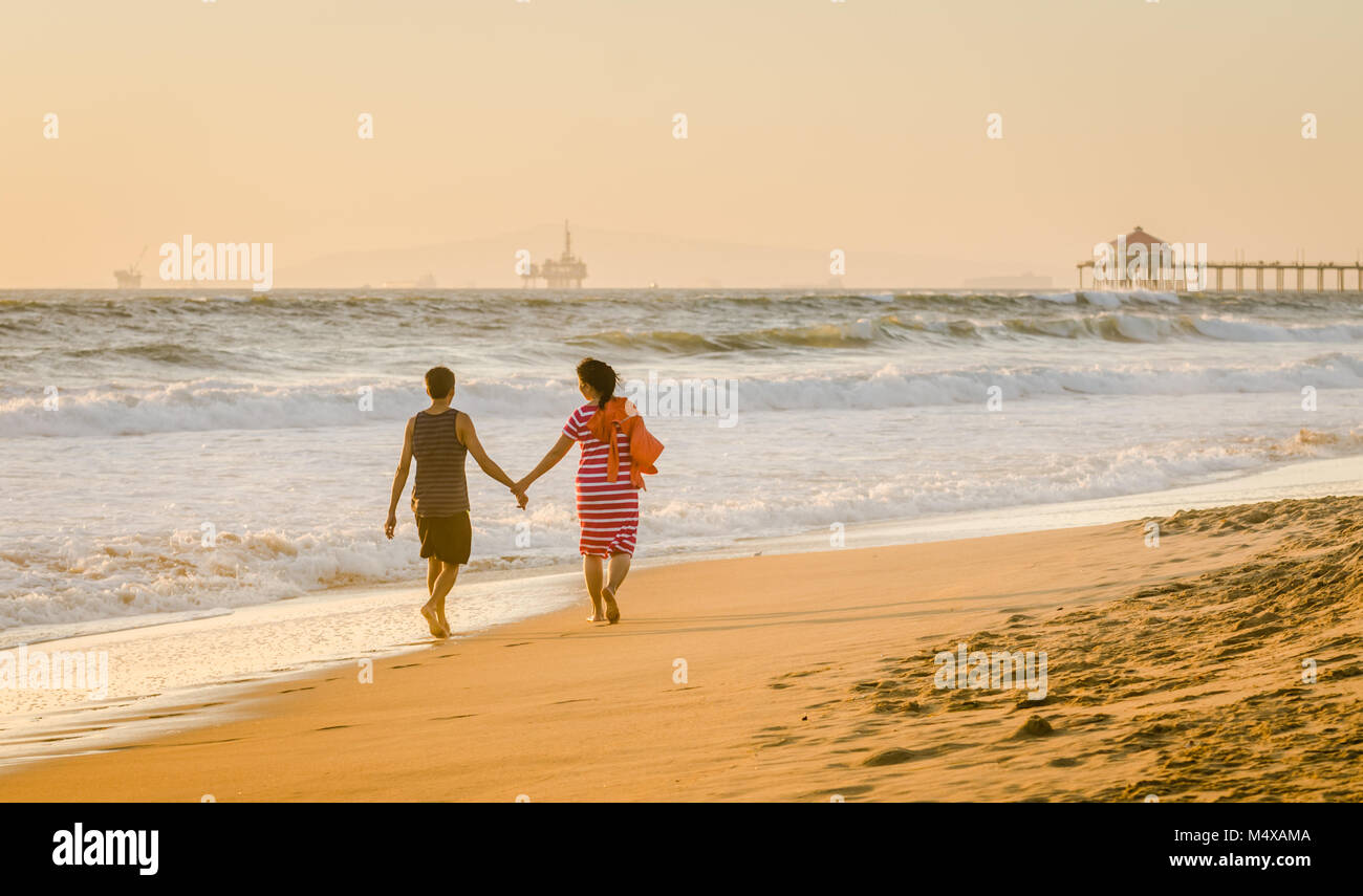 A couple takes a golden hour stroll on the shore edge at Huntington Beach in California. Stock Photo