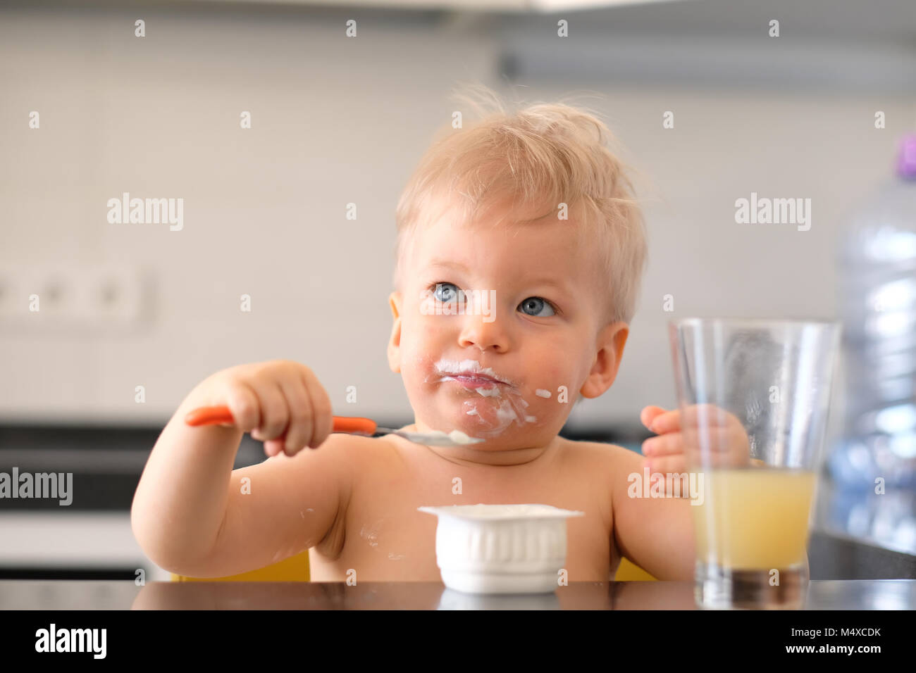 Adorable one year old baby boy eating yoghurt with spoon Stock Photo