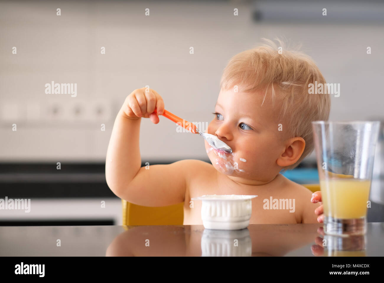 Adorable one year old baby boy eating yoghurt with spoon Stock Photo