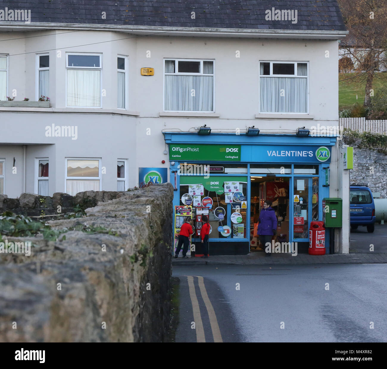 A street scene with people and children outside a rural supermarket.  in Ireland Two schoolgirls outside  XL shop, Carlingford County Louth Ireland. Stock Photo