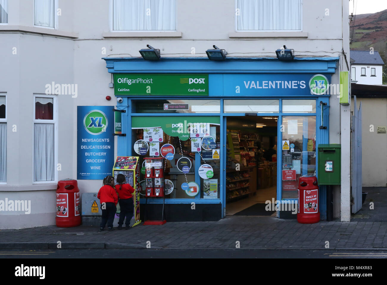 Children outside a supermarket and post office in rural Ireland. The XL brand supermarket is in Carlingford County Louth Ireland. Stock Photo