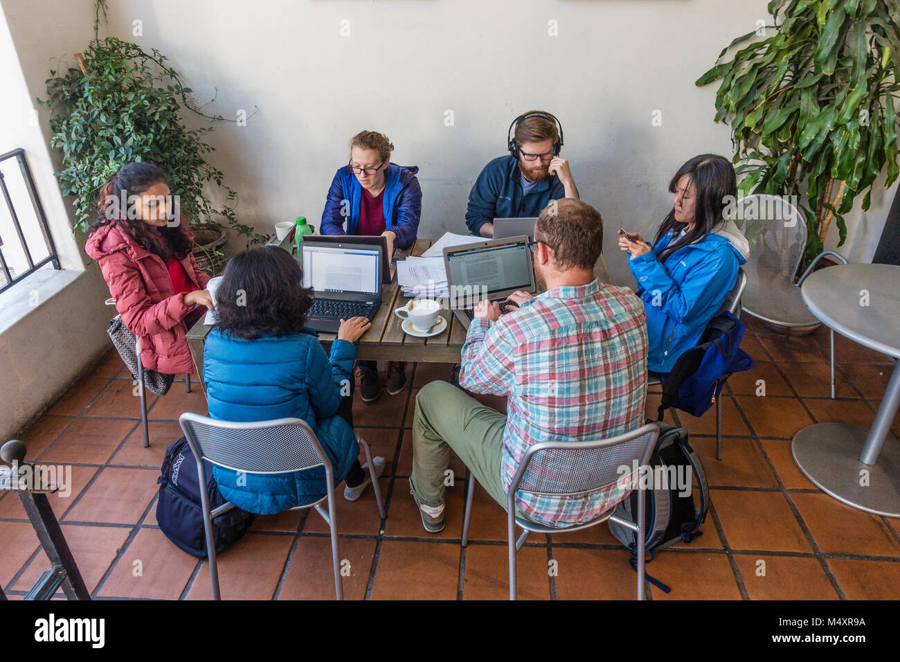 A group of six college students sit at a table at a coffee shop patio studying together with