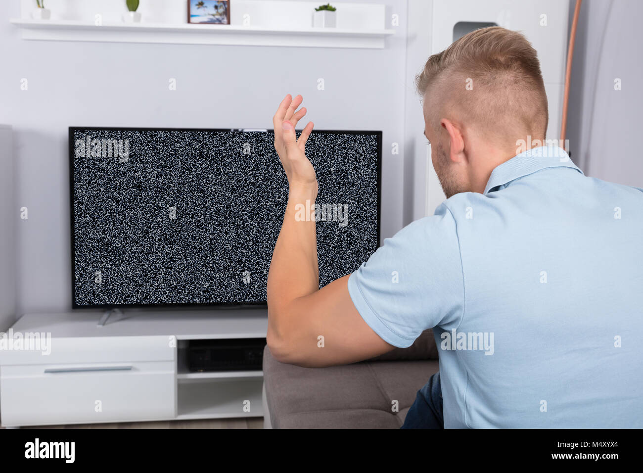 Frustrated Man Sitting On Sofa In Front Of Television With No Signal Stock Photo