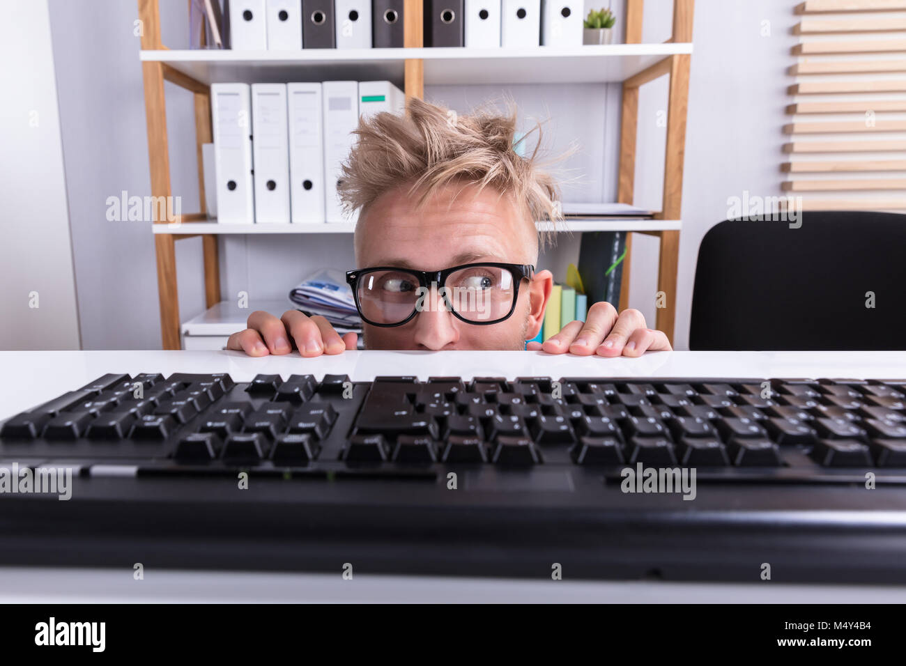 Funny Businessman Wearing Eyeglasses Hiding Behind Desk In Office Stock Photo