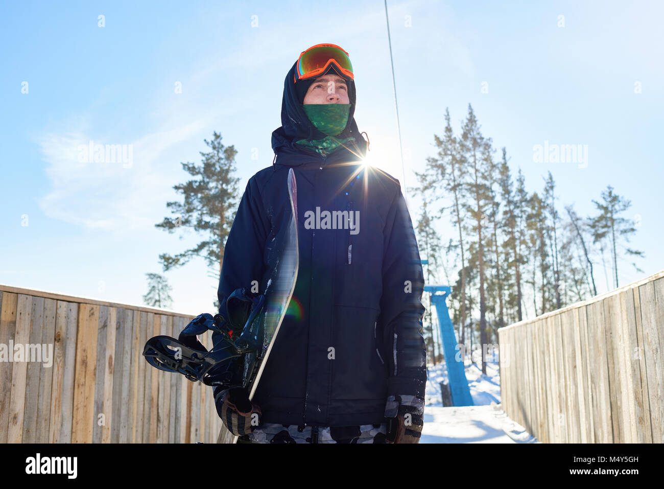 Low angle portrait of modern young man holding snowboard and looking ...