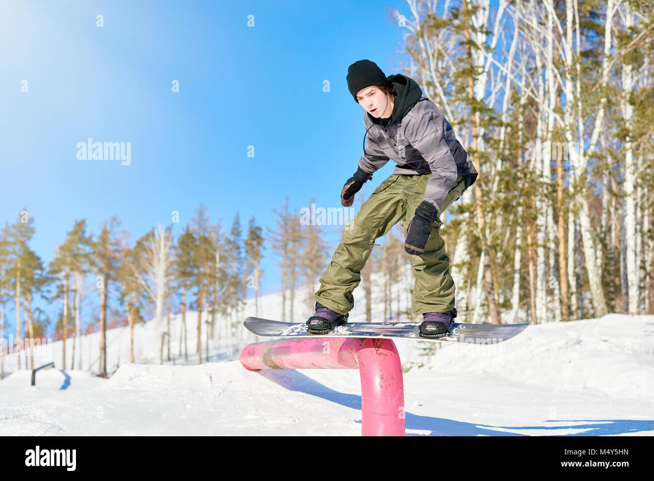 Full length action shot of young man performing snowboarding stunt sliding  down metal railing in sunlight at ski resort, copy space Stock Photo - Alamy