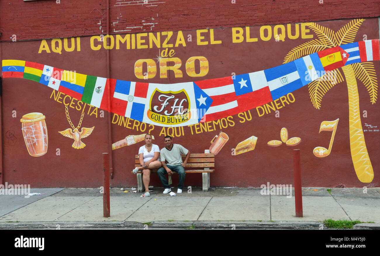 Hispanic couple sits on bench in front of Golden Block Mural in Philadelphia, PA, USA. Stock Photo