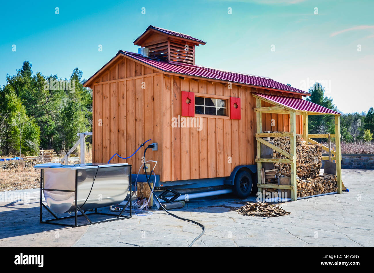 Mobile sugar shack on wheels with red maple leaf shutters and a stainless steel evaporator set outdoors. Stock Photo