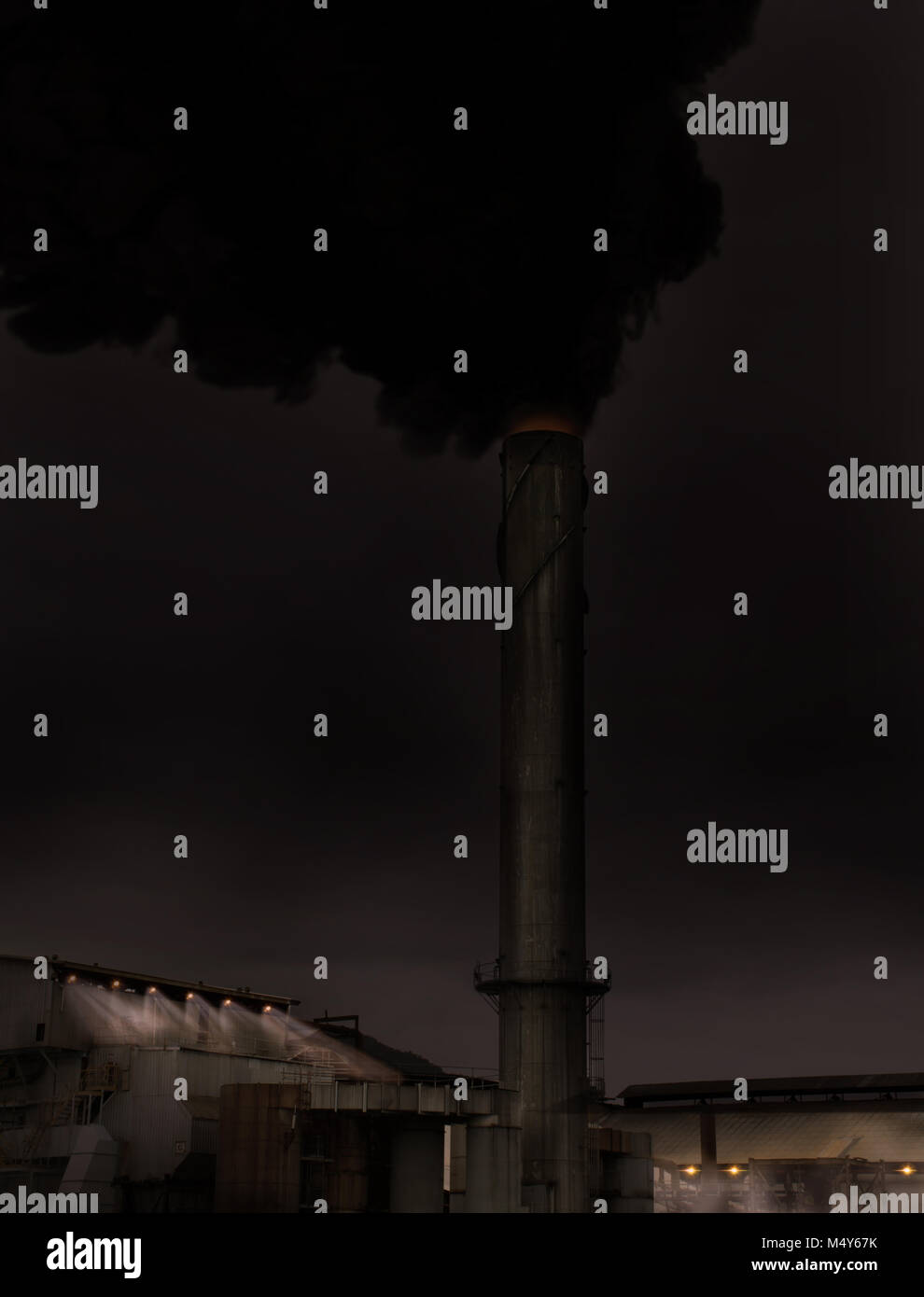 A sinister looking factory night scene with smoke billowing from a tall exhaust stack and lights in the mist Stock Photo