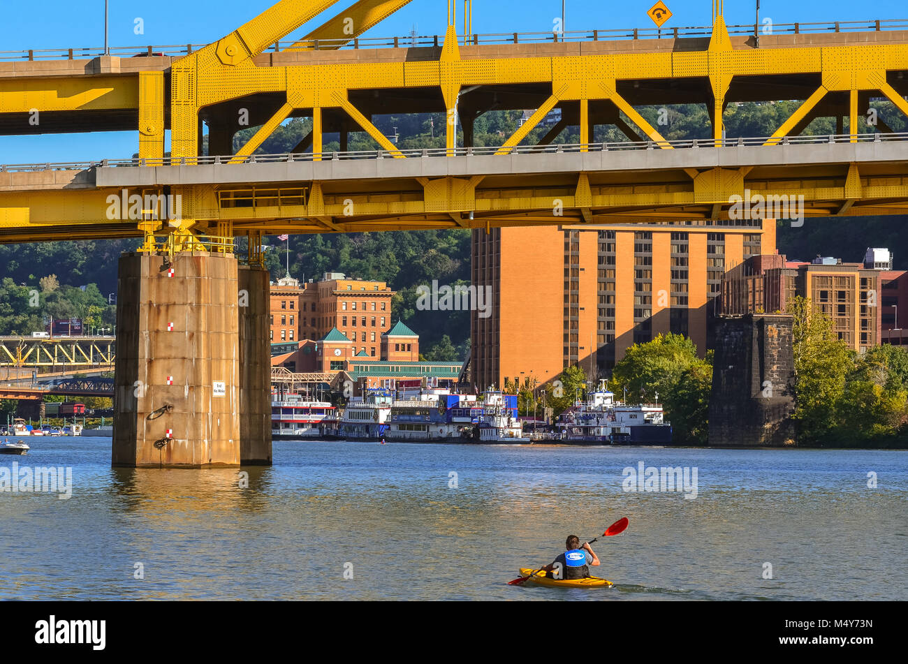 A lone man rows a kayak on the Ohio River under a yellow bridge in Pittsburgh, Pennsylvania. Stock Photo