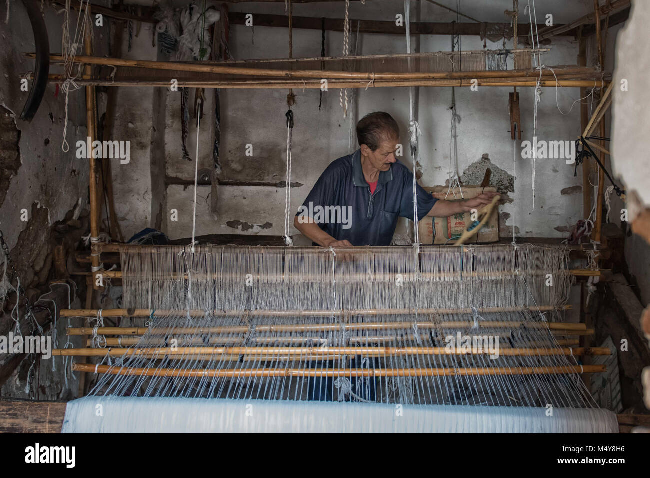 A local Moroccan man weaves on an old bamboo loom in the medina of Marrakech, Morocco. The loom takes up almost the entire room in the man's room. Stock Photo
