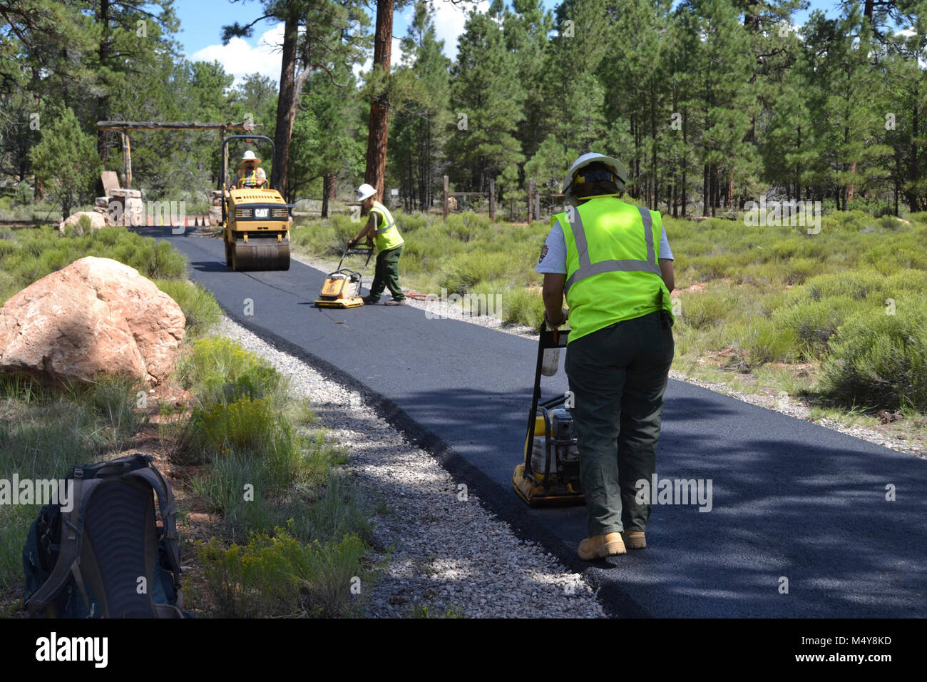 Workers smooth asphalt with paving machines.  Between August 10 to September 10, 2016 the Greenway Trail between the IMAX Theater parking area in Tusayan and Center Road in Grand Canyon National Park will be closed while Grand Canyon's trail crew installs asphalt. The portion of the trail north of Center Road will not be affected.  While the trail closure is in effect, cyclists and hikers may ride the Tusayan shuttle (Purple Route) which is equipped with bicycle carrier racks. The shuttle connects Tusayan with the South Rim Visitor Center, a 20 minute ride each way.  The intent of this project Stock Photo
