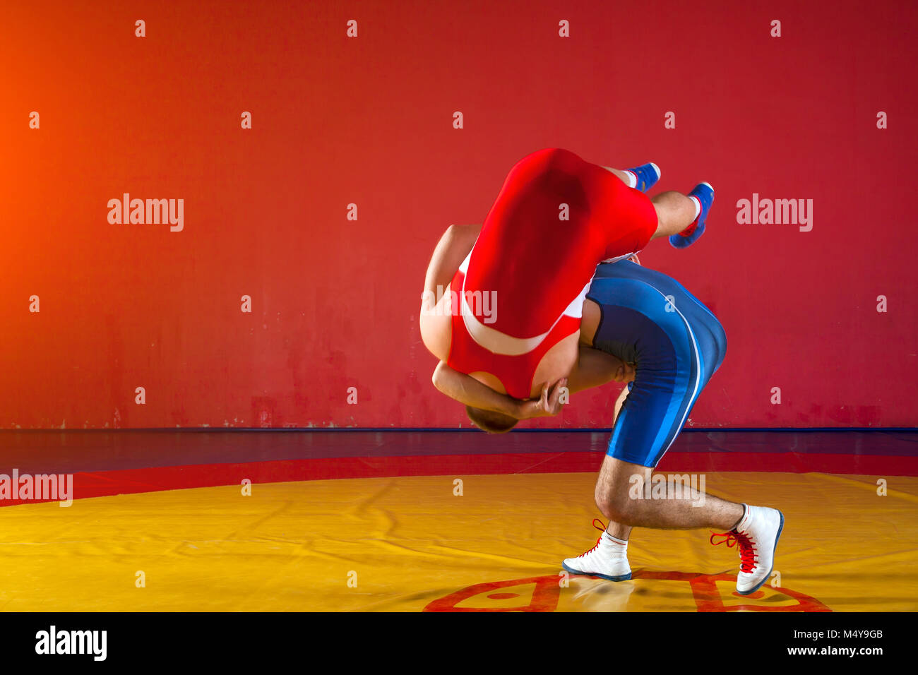 Two strong wrestlers in blue and red wrestling tights are wrestlng and