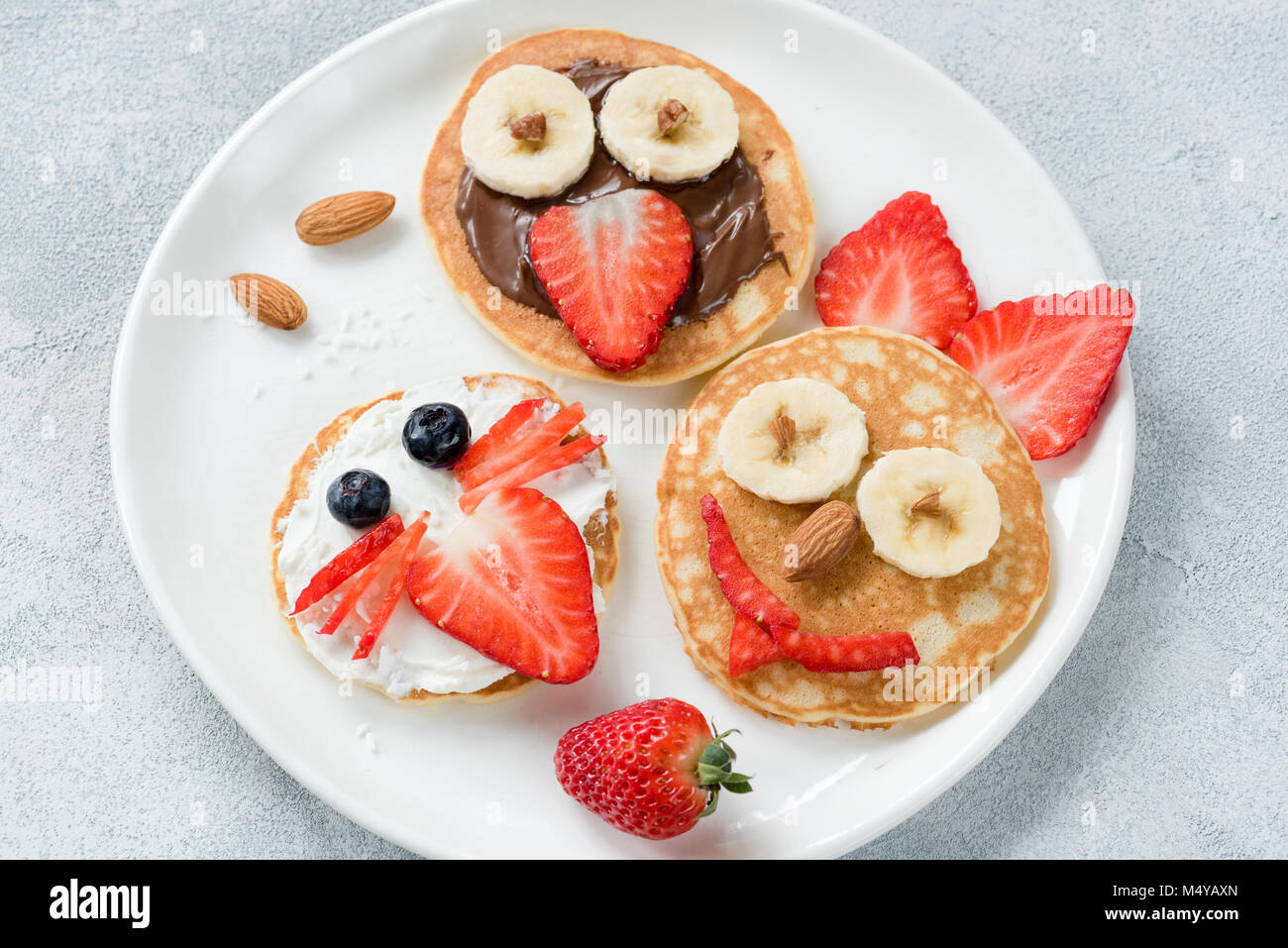 Funny colorful breakfast pancakes with animal faces for kids on white plate. Top view Stock Photo