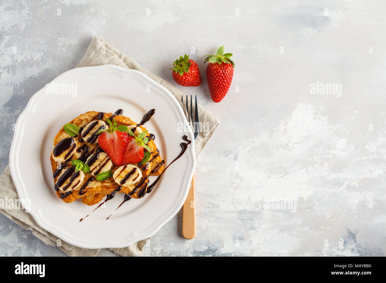 French toasts with chocolate syrup, strawberries and a banana. Gray background, copy space, top view. Stock Photo