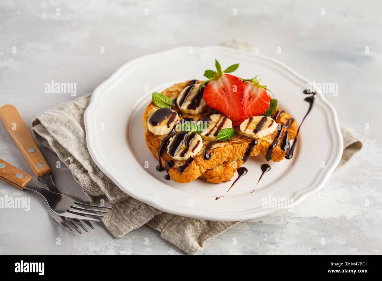 French toasts with chocolate syrup, strawberries and a banana. Gray background, copy space, top view. Stock Photo