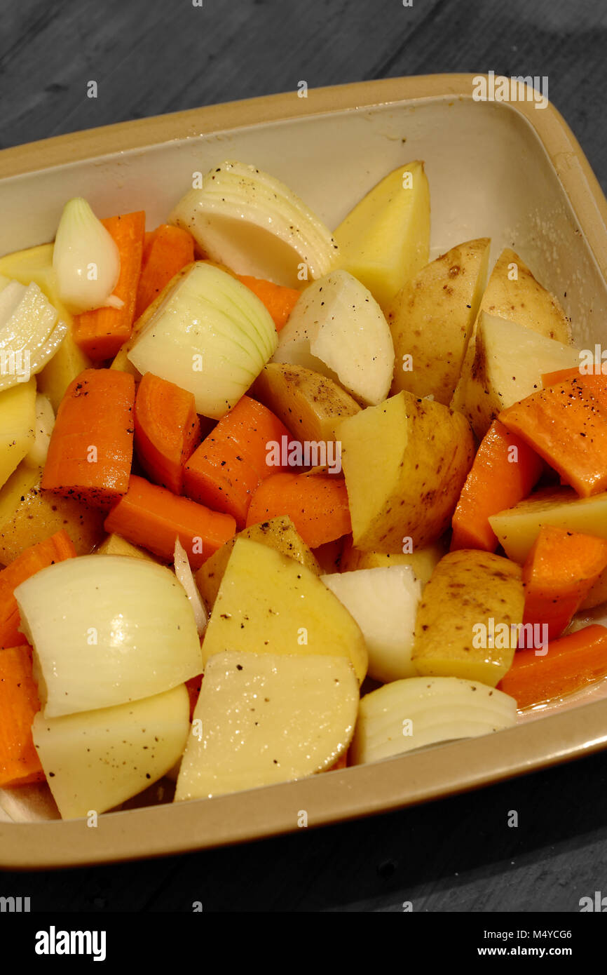 Raw carrot, onion and potato in a ceramic dish prepared for roasting
