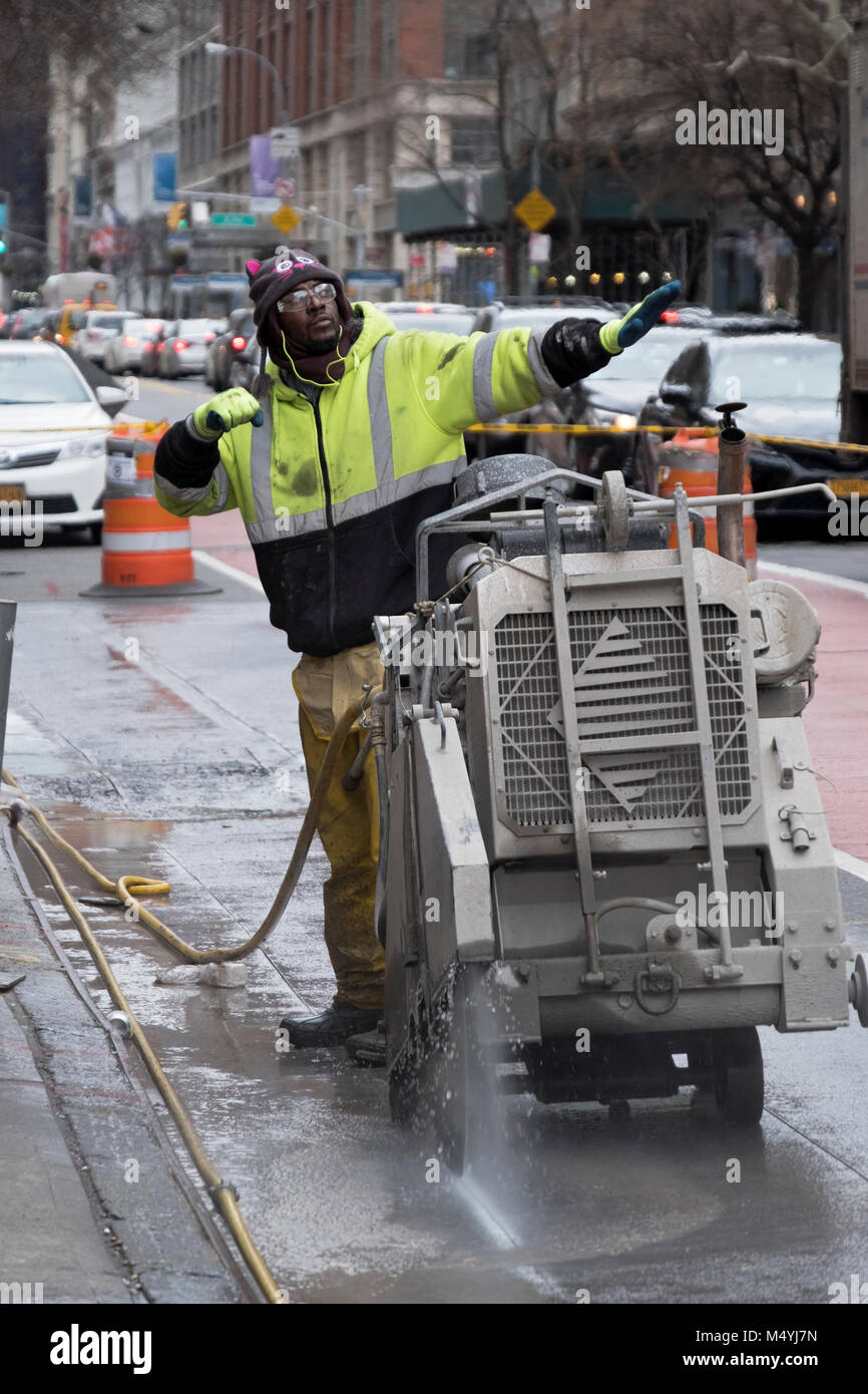 A construction worker on West 23rd Street in Manhattan cutting through the pavement to get to the electrical lines which will be upgraded. Stock Photo