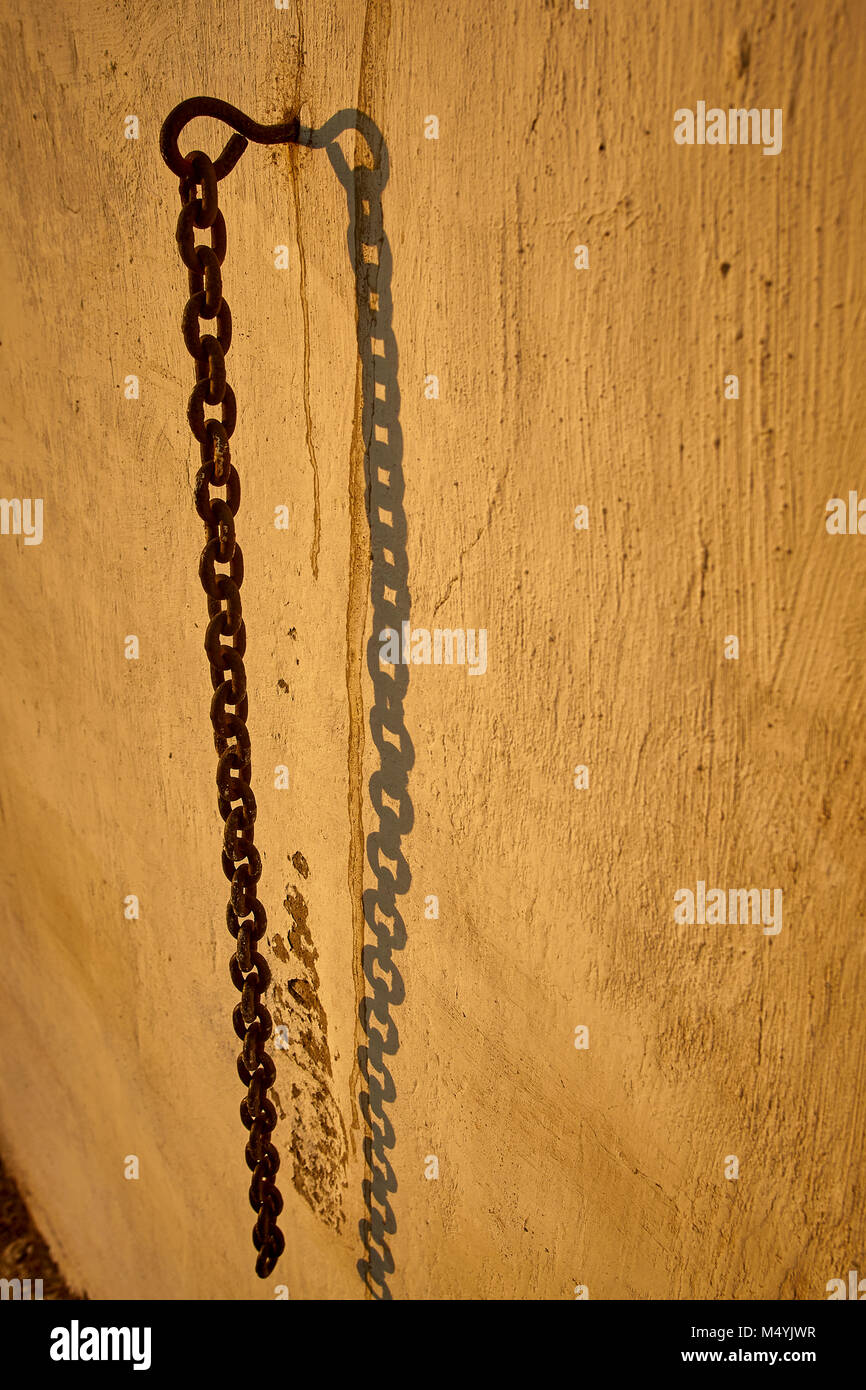 Old iron chain hanging from a peg in a stucco brick wall Stock Photo