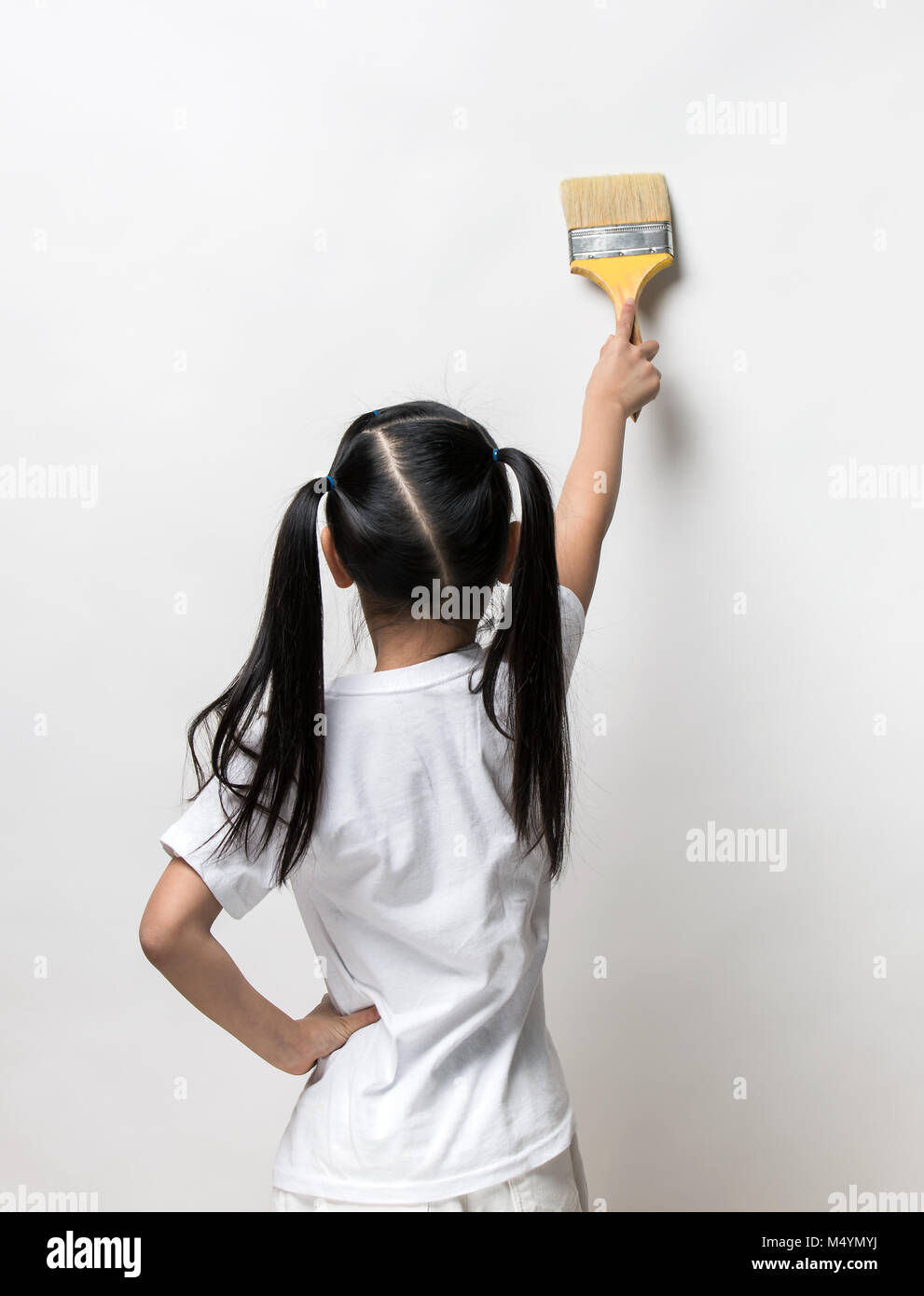 Little girl drawing something using painting brush on wall background Stock Photo
