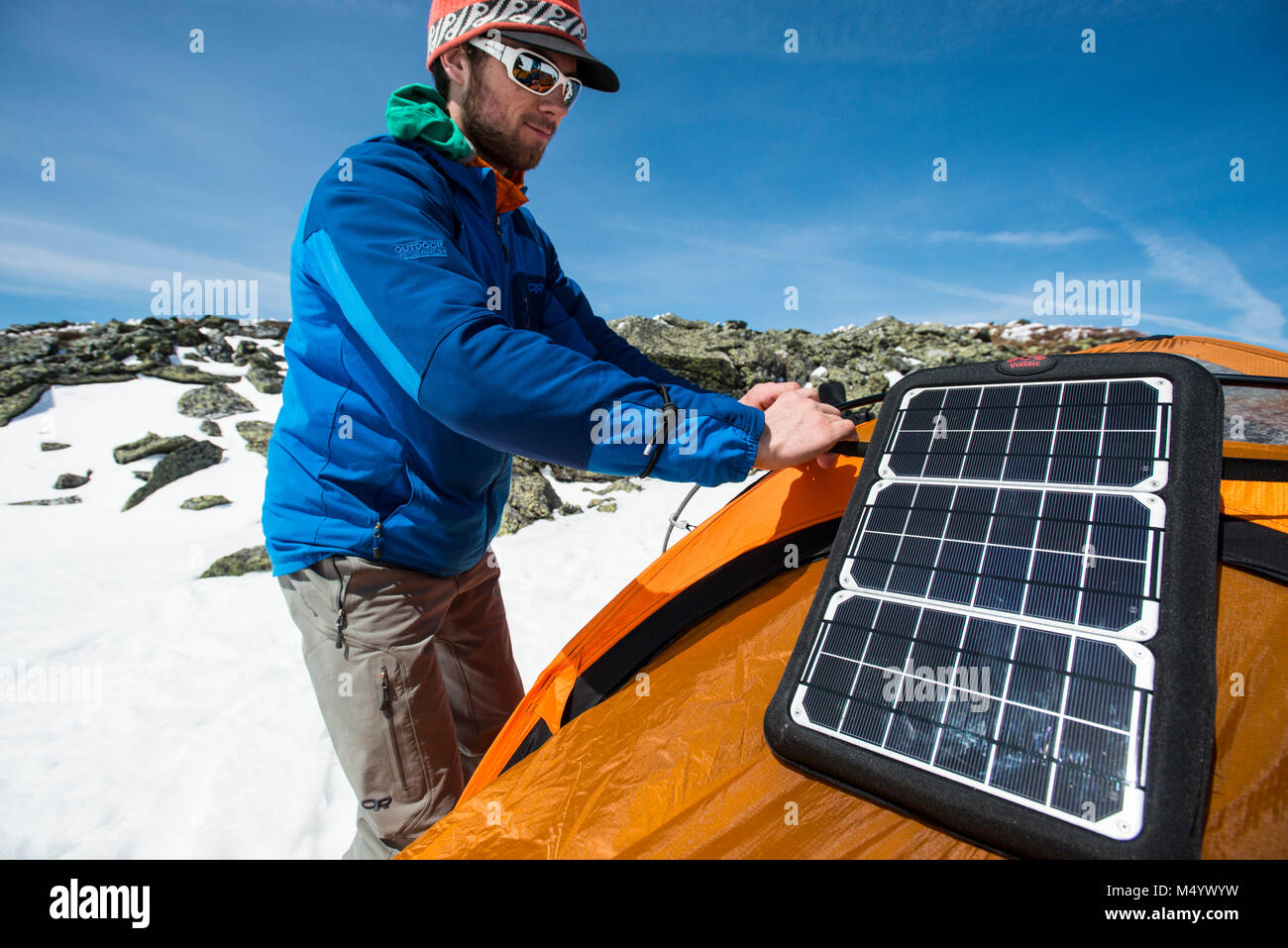 Man installing solar panel on tent before camping in winter in White Mountains, New Hampshire, USA Stock Photo