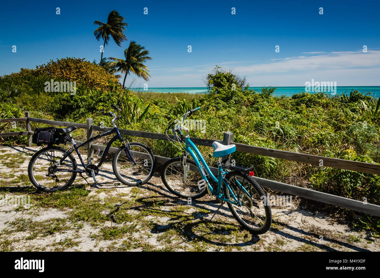 Two bicyles, one with a saddle bag, sit parked by a wooden fence on the beach at Bahia Honda State Park in the Florida Keys. Stock Photo