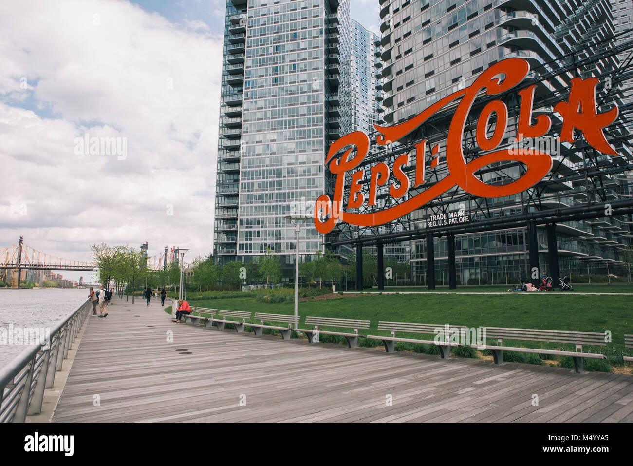 People on promenade boardwalk near iconic sign in Gantry Plaza State Park with view of Queensborough Ed Koch Bridge in distance, Long Island City, New York City, USA Stock Photo