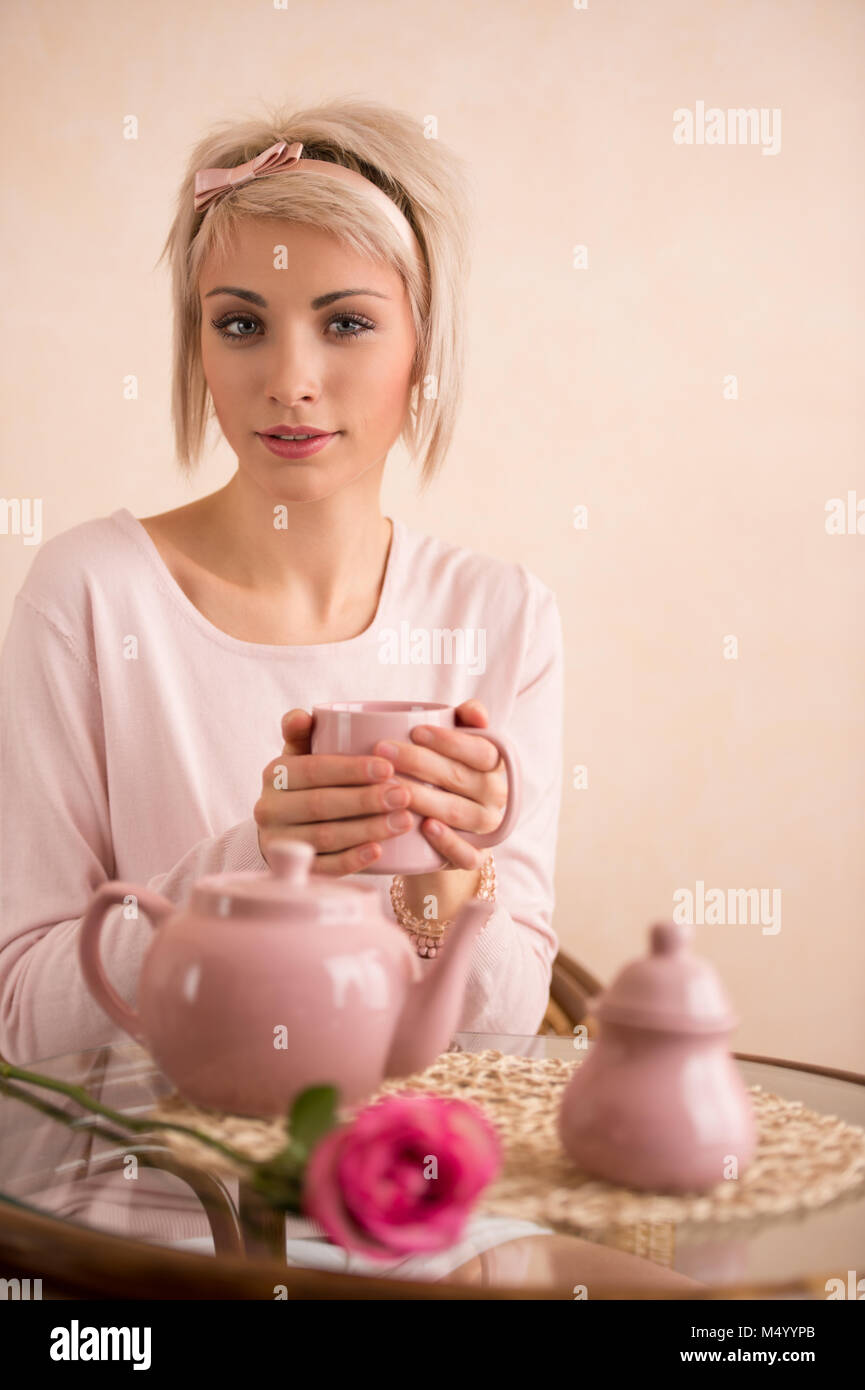 Young beautiful woman having teaparty in pink feminine style. She is
