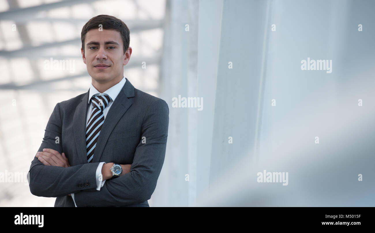 Portrait of handsome confident young businessman standing arms crossed ...