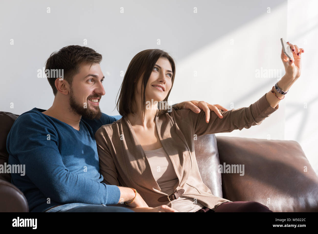 Cheerful couple taking a selfie with a smartphone at home sitting on ...