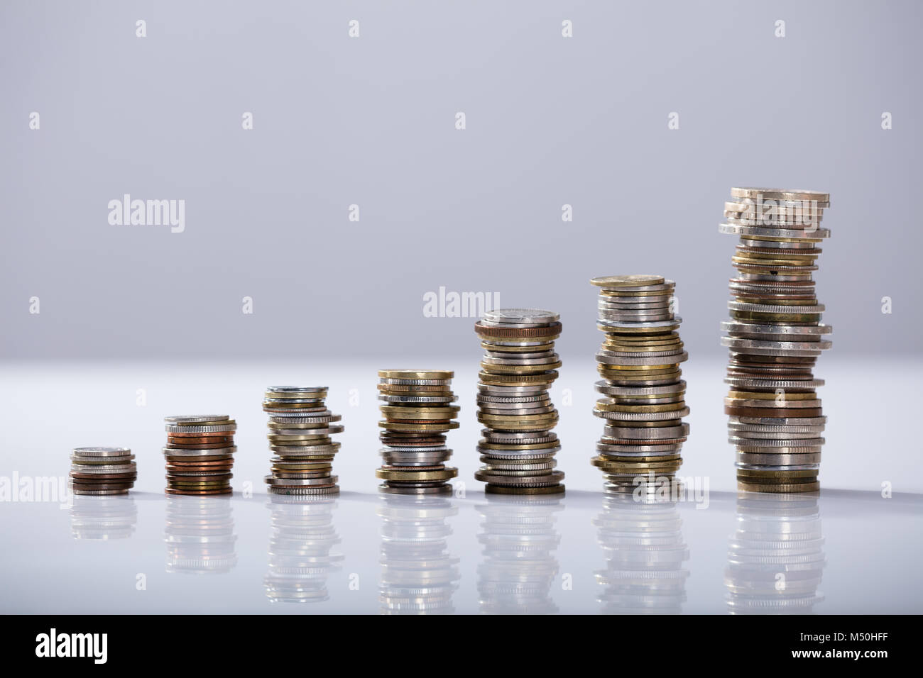 Increasing Stack Of Coins On The Reflective Desk Over White Background ...