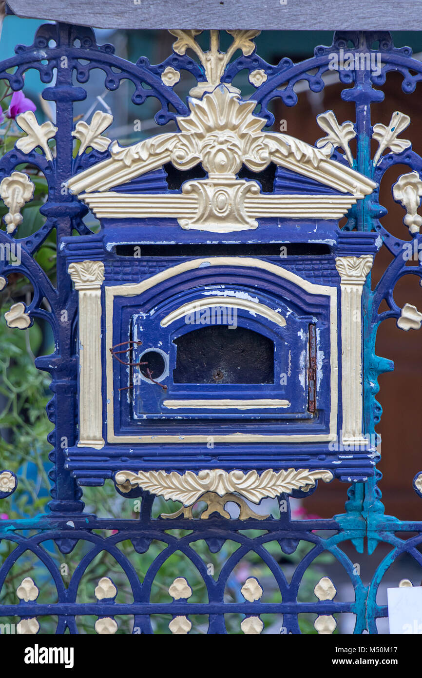 A old empty decorative mailbox on fence. Blue domestic post-box with ornaments on iron gate. Stock Photo