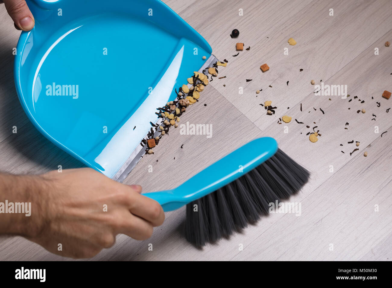 Close-up Of Male Sweeping Wooden Floor With Small Whisk Broom And Dustpan Stock Photo