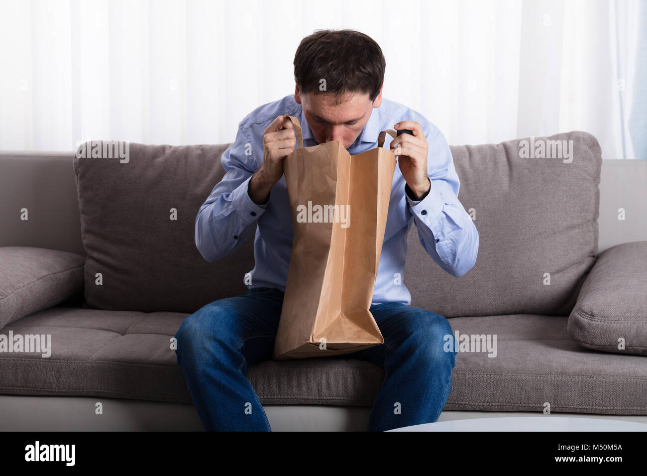 A Man Sitting On Sofa Vomiting Into Paper Bag At Home Stock Photo - Alamy