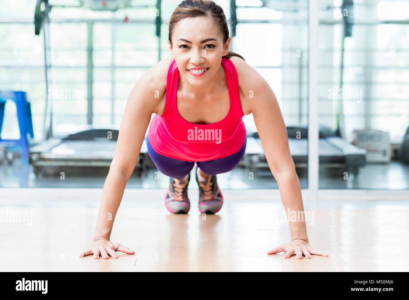 Smiling young woman doing pushup in gym Stock Photo