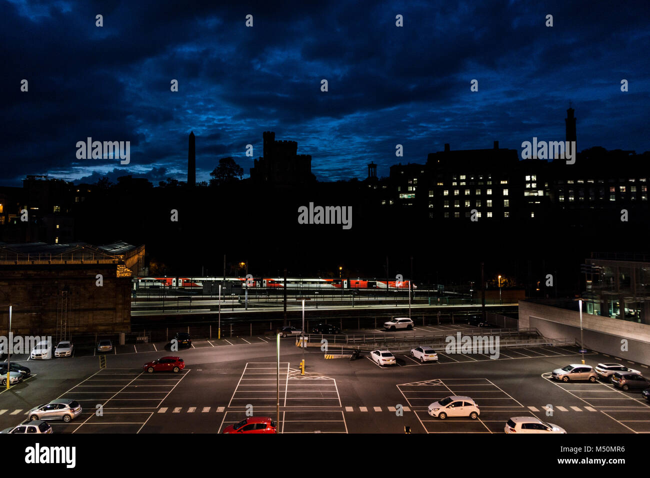 A car park at Edinburgh Waverley Station at night against a silhouetted