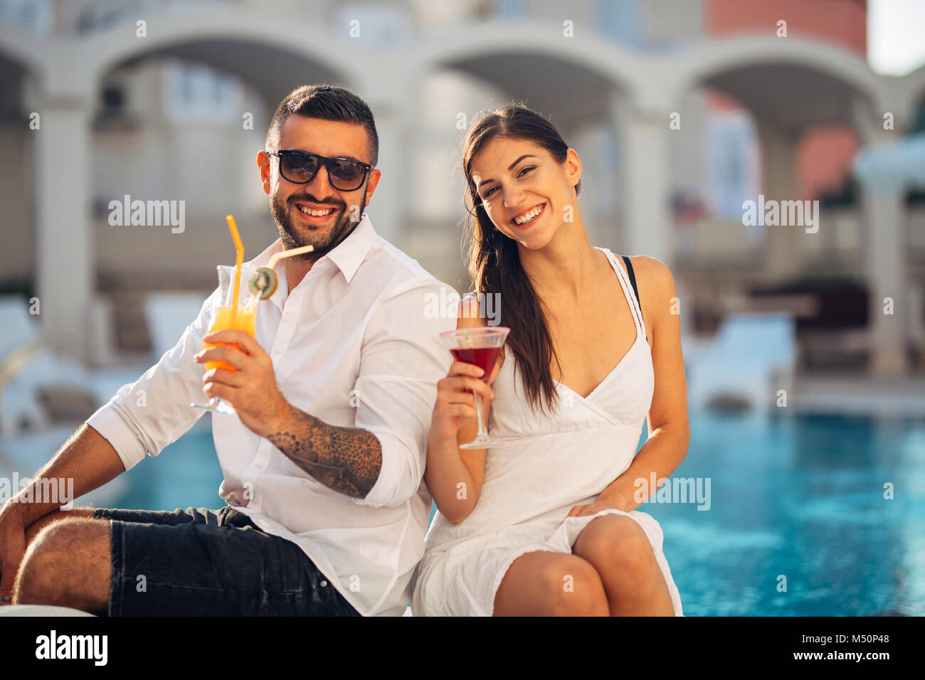 Attractive couple enjoying summer vacation near the pool in exotic vacation resort.Attending summer pool longe bar party,beach party.Drinking refreshi Stock Photo