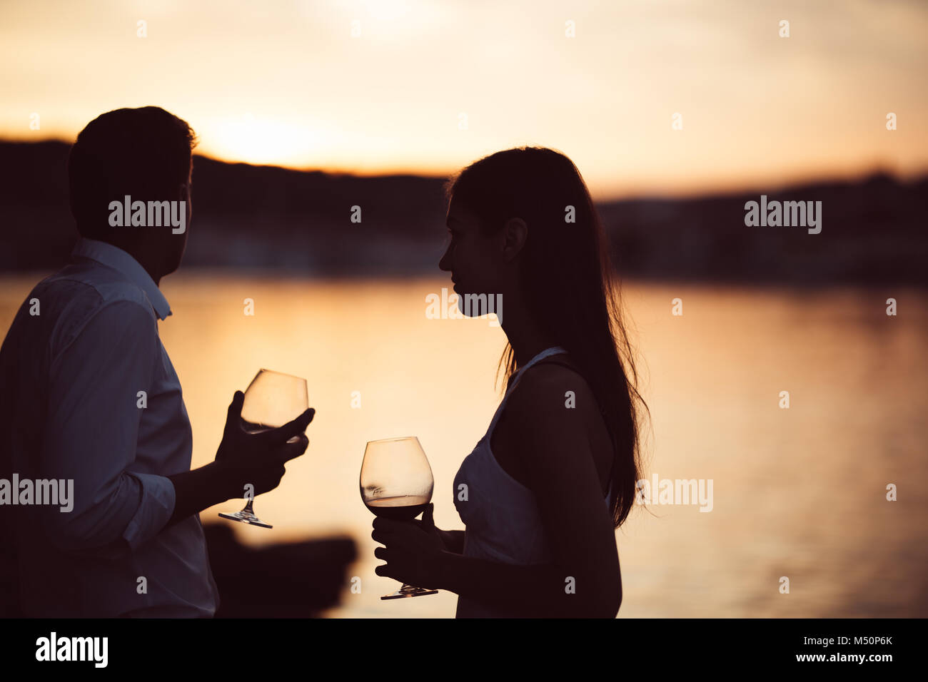 Two young people enjoying a glass of red wine in the sunset on the seaside.Healthy glass od homemade red wine,Mediterranean culture.Warm climates,seas Stock Photo