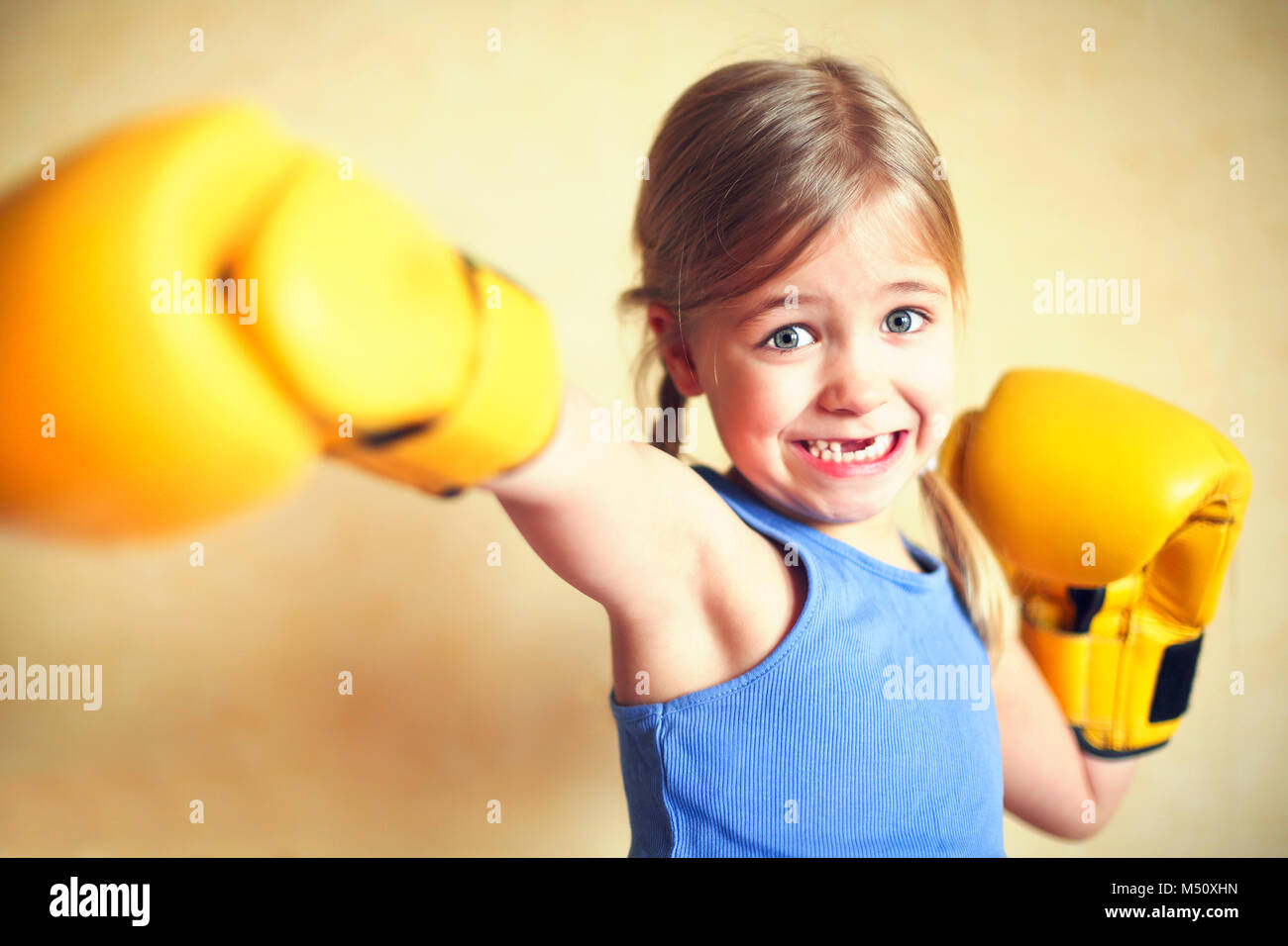 Little girl with yellow boxing gloves over yellow wall background. Girl power concept. Funny little kid portrait. Happy lost tooth little girl portrai Stock Photo