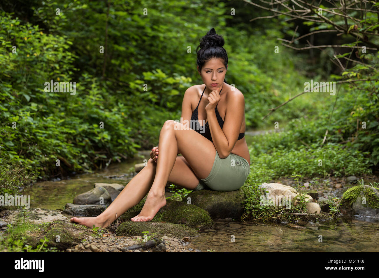 Young woman sitting on a stone in stream Stock Photo