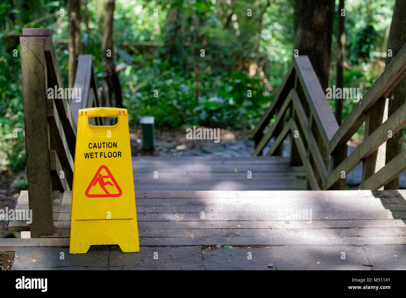 Yellow Caution slippery wet floor sign outdoors near wooden staircase Stock Photo