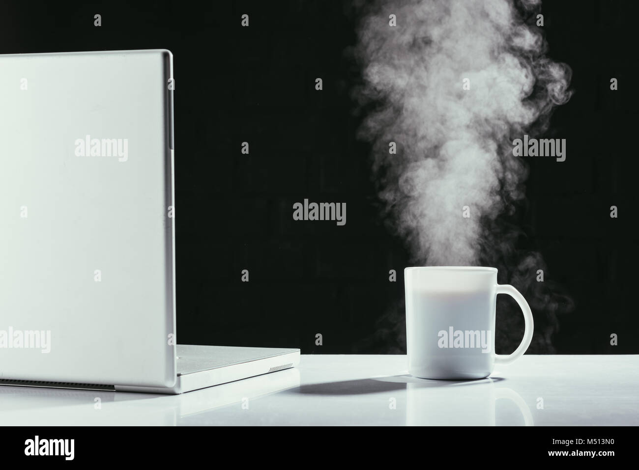 laptop with steaming cup of tea on table isolated on black Stock Photo ...