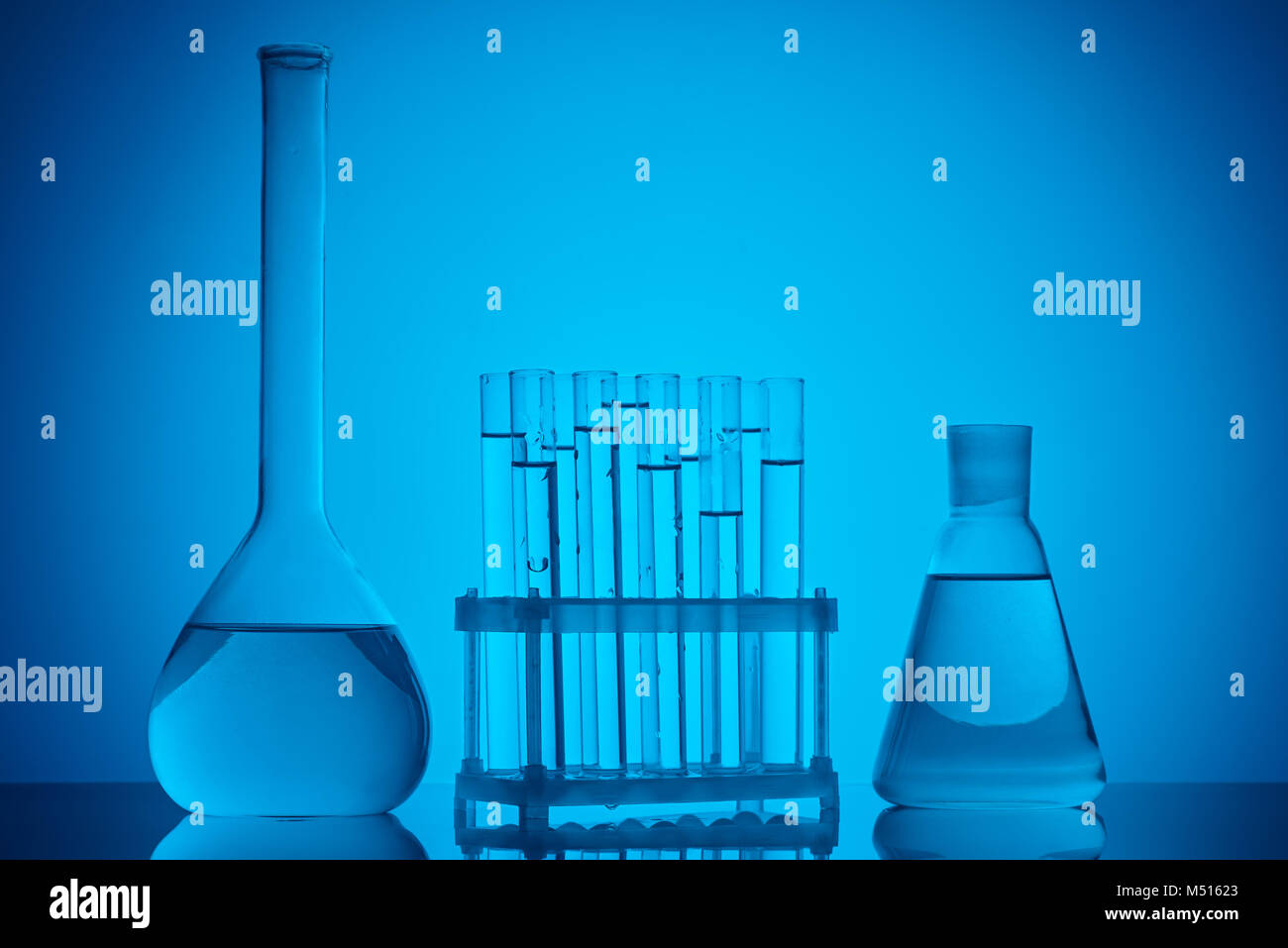 glass tubes on stand and glass flasks with liquid on table on blue ...