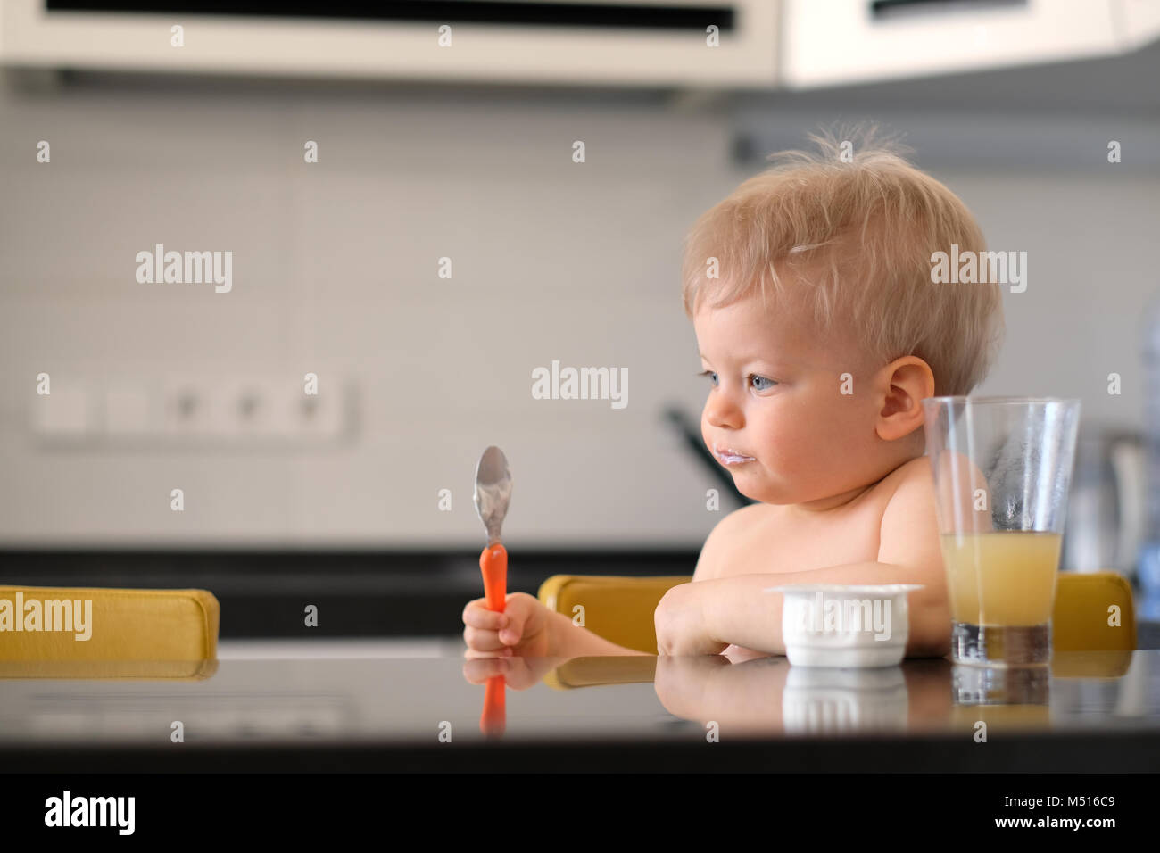 Adorable one year old baby boy eating yoghurt with spoon Stock Photo